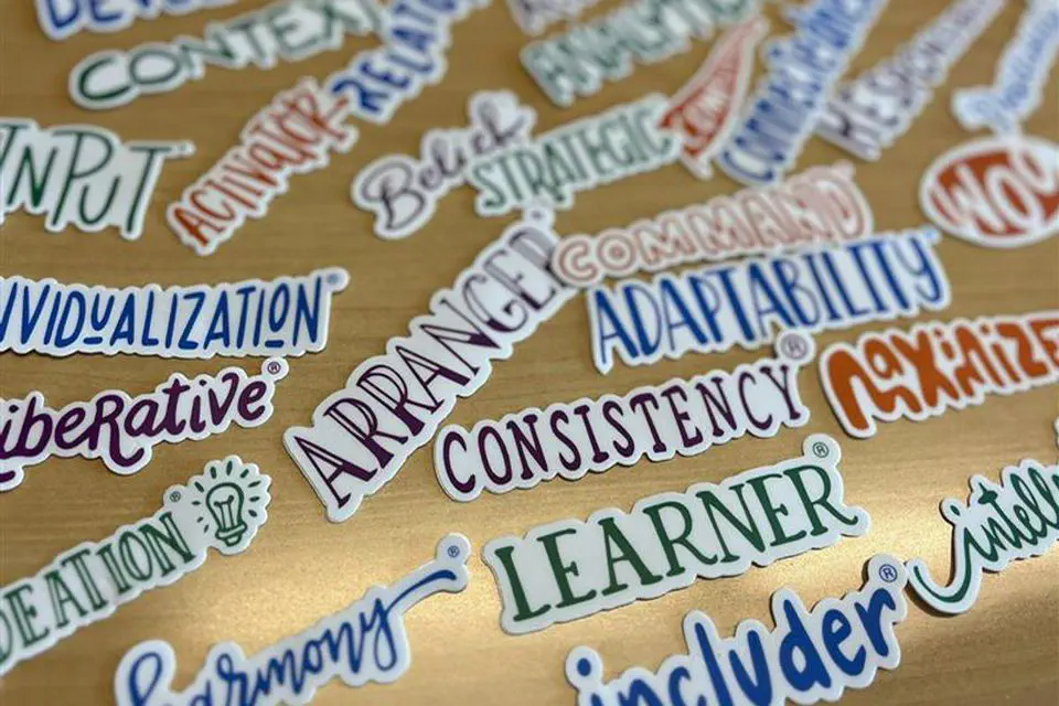 The image displays a collection of motivational and personality trait stickers scattered on a wooden surface.