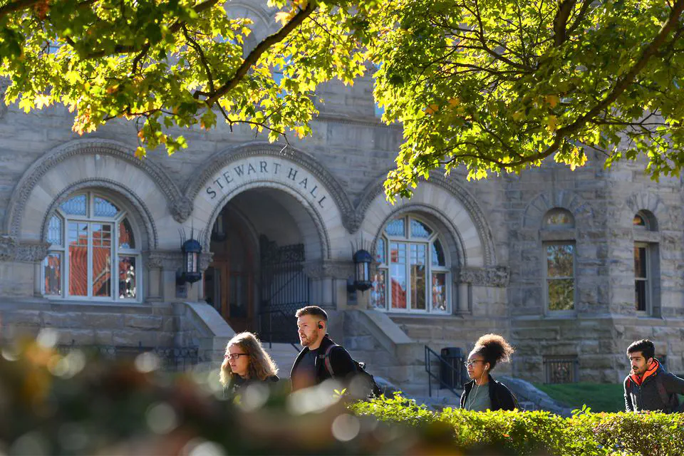 A group of students walks in front of a stone building on a sunny day.