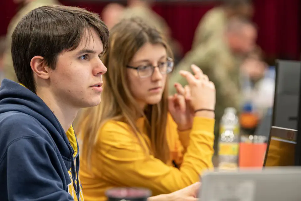 The image shows two young people intently focused on something in front of them, possibly a competition or collaborative task.